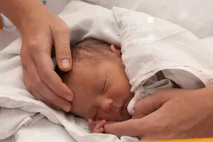 Baby im Bett, das von einem Erwachsenen behutsam überprüft wird